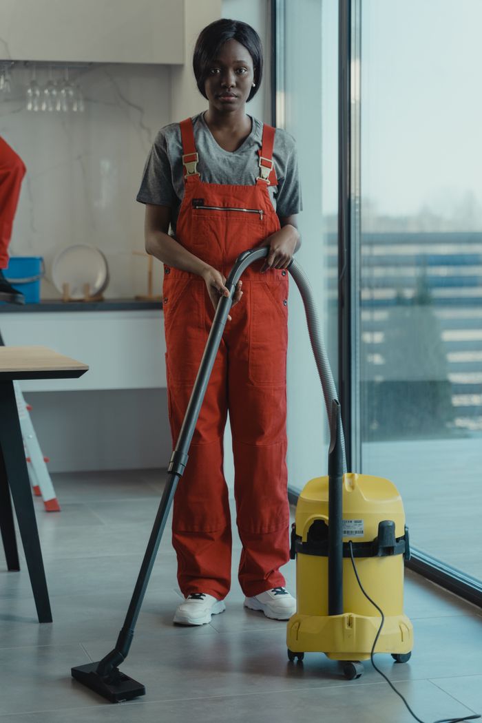 Une femme adulte vêtue d’une combinaison rouge utilise un aspirateur dans un intérieur moderne, concentrée sur des tâches de nettoyage.